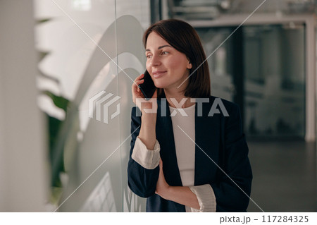 A successful businesswoman smiling while talking on the phone in a modern office A successful businesswoman smiling while talking on the phone in a modern office 117284325