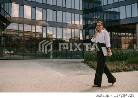 A confident businesswoman walking outside a modern office building, showcasing her style 117284329