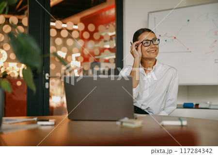 A Professional Woman in a Modern Office Working Diligently with a Laptop and Stylish Glasses A Professional Woman in a Modern Office Working Diligently with a Laptop and Stylish Glasses 117284342