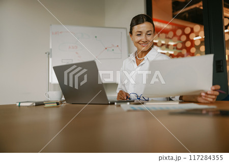A businesswoman meticulously reviewing various reports in a modern, hightech office space 117284355