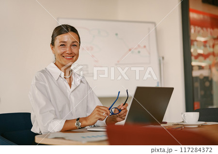 A Smiling Businesswoman at a Contemporary and Modern Workspace Engaged in Her Work 117284372