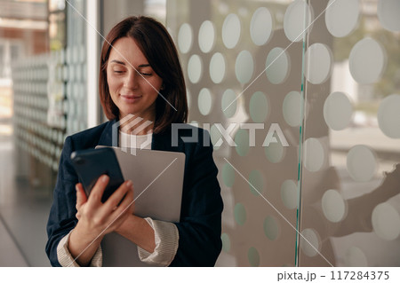 A businesswoman is shown multitasking by using a smartphone along with a tablet 117284375