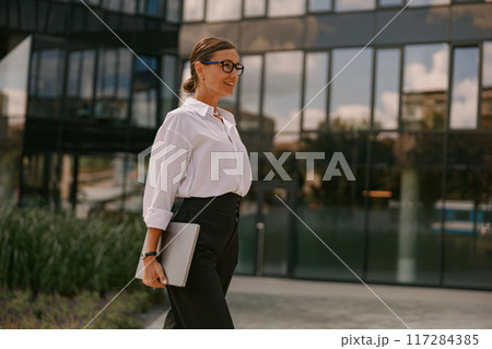 A Professional Woman confidently walking in a Modern Urban Environment, embodying success 117284385