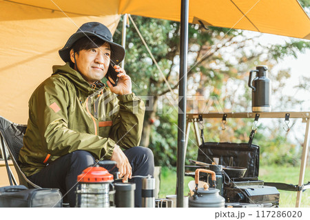 キャンプ場でスマホを使う中年男性キャンパー(キャンプ場・通話・話す) キャンプ場でスマホを使う中年男性キャンパー(キャンプ場・通話・話す) 117286020