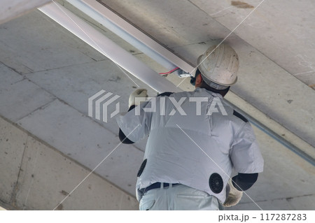 電気工事　階段の天井に照明器具を取り付ける作業員 117287283