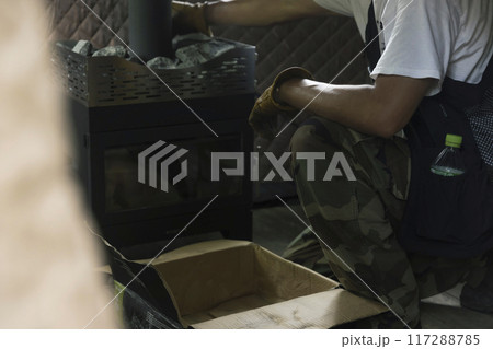 テントサウナ用の薪ストーブの上にサウナストーンを乗せる男性 117288785