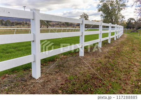 A white metal fence on the outer perimeter of a local horse racing track A white metal fence on the outer perimeter of a local horse racing track 117288885