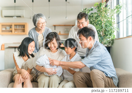 家のソファで赤ちゃんを抱っこするママと三世代家族・ファミリー 家のソファで赤ちゃんを抱っこするママと三世代家族・ファミリー 117289711