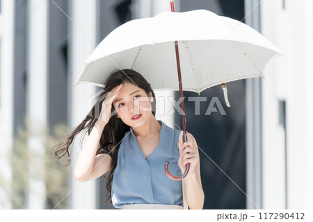 オフィス街で暑そうに日傘をさして歩くビジネスウーマン オフィス街で暑そうに日傘をさして歩くビジネスウーマン 117290412