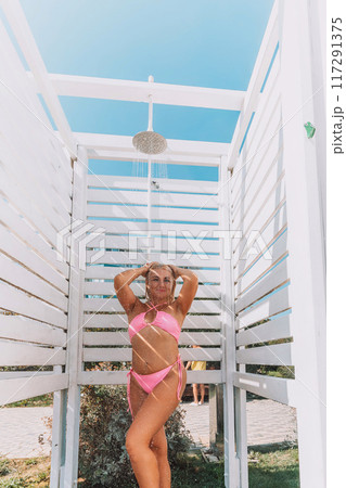 A woman in a bikini stands in front of a white shower stall. She is smiling and she is enjoying the moment 117291375
