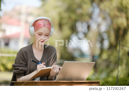 Young woman with a laptop and notes studying in the park for education in nature to relax and learn online. 117292267