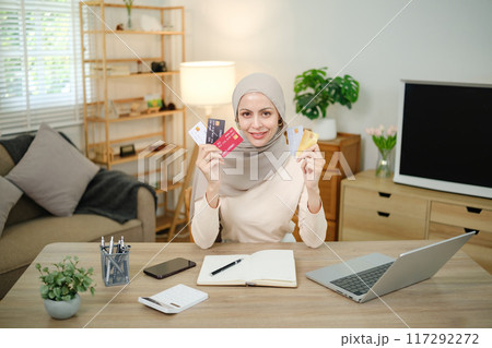 A woman is holding a credit card and a laptop on a desk 117292272