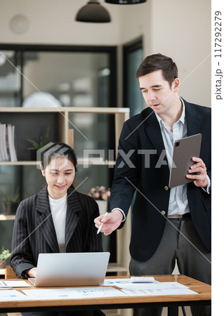A man and a woman are standing in front of a laptop computer 117292279