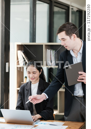 A man and a woman are standing in front of a desk with a laptop and a tablet A man and a woman are standing in front of a desk with a laptop and a tablet 117292280