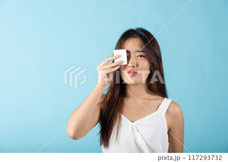 Facial Beauty Treatment Hygiene skin. Asian beautiful young woman removing cosmetic make up using pad cotton face cleaner disc, studio shot isolated on blue background, Happy female cleaning eyes 117293732