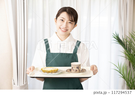 笑顔でコーヒーとケーキを運ぶカフェの女性スタッフ 117294537