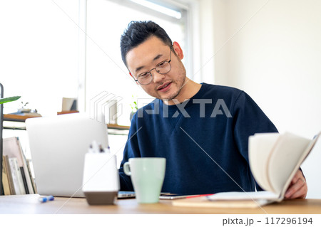 パソコン作業をしながら手書きのノートを確認している男性 パソコン作業をしながら手書きのノートを確認している男性 117296194