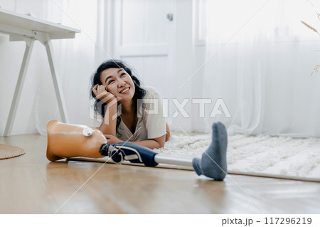 Woman with trying catch prosthetic leg on floor 117296219