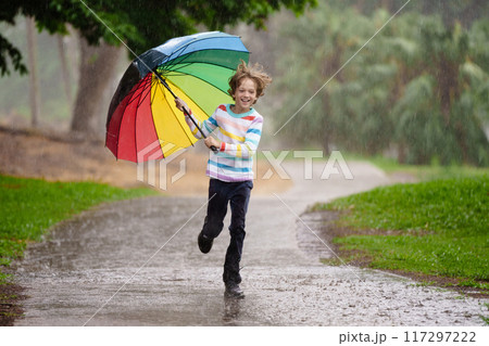 Child playing in rain. Kid jumping in puddle. 117297222