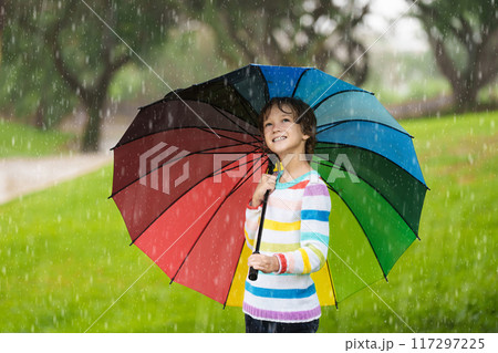 Child playing in rain. Kid jumping in puddle. 117297225