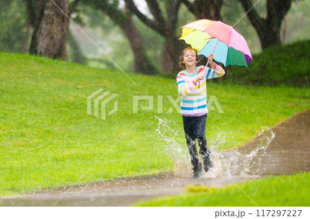 Child playing in rain. Kid jumping in puddle. 117297227