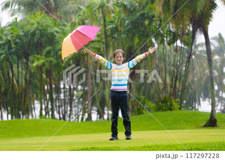 Child playing in rain. Kid jumping in puddle. 117297228