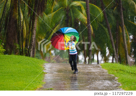 Child playing in rain. Kid jumping in puddle. 117297229