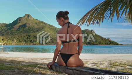 Woman peacefully enjoys the warm sun and breathtaking view on a secluded beach in maupiti. French polynesia. Creating an idyllic paradise perfect for relaxation and soaking up the beauty of nature Woman peacefully enjoys the warm sun and breathtaking view on a secluded beach in maupiti. French polynesia. Creating an idyllic paradise perfect for relaxation and soaking up the beauty of nature 117298150