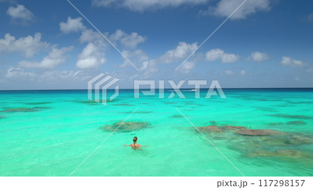 Woman swimming in crystal turquoise sea water under blue clouds sky in sunny day. Tourist girl relax and enjoy outdoor lifestyle travel on summer holiday vacation. Aerial view drone 117298157