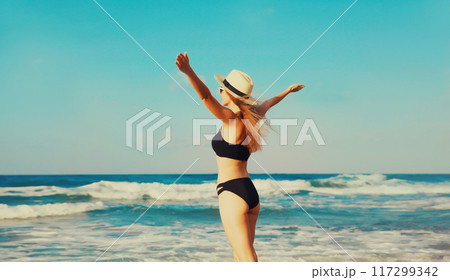 Summer vacation, beautiful happy woman in bikini swimsuit raising her hands up on the beach on sea 117299342
