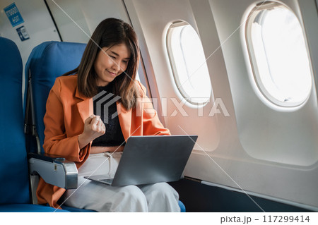 A young businesswoman working on her laptop while traveling on an airplane, showing focus and determination. 117299414