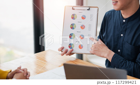 Professional business meeting with a focus on a clipboard displaying colorful pie charts, highlighting data analysis and teamwork. Professional business meeting with a focus on a clipboard displaying colorful pie charts, highlighting data analysis and teamwork. 117299421