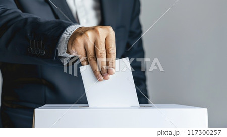 Civic duty - hand placing a ballot paper in ballot box for voting, emphasizing importance of election concept, showcasing anonymity of secret ballot, reflecting competitive nature of preelection race. Civic duty - hand placing a ballot paper in ballot box for voting, emphasizing importance of election concept, showcasing anonymity of secret ballot, reflecting competitive nature of preelection race. 117300257
