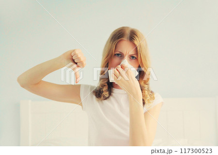 Portrait of sick upset woman sneezing blow nose using tissue 117300523