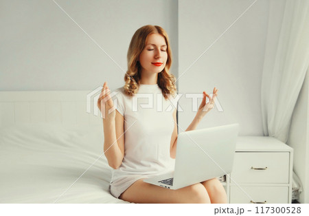 Relaxed young woman taking a break for breathing exercises working with laptop on the bed Relaxed young woman taking a break for breathing exercises working with laptop on the bed 117300528