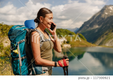 A woman is hiking in beautiful nature with her backpack and mobile phone in hand A woman is hiking in beautiful nature with her backpack and mobile phone in hand 117300921