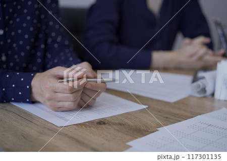 Accountants or auditors reviewing financial documents while sitting at the wooden desk in office. Professionals analyzing paper reports and using calculators, view above. Audit and taxes concept 117301135