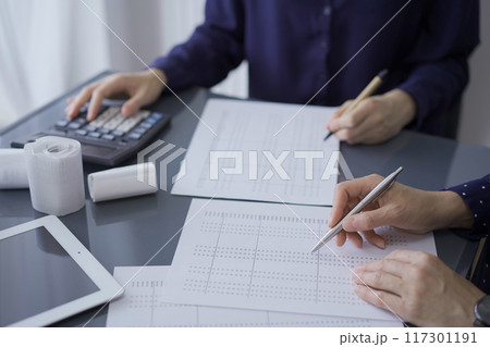 Two unrecognizable female accountants or auditors are sitting and reviewing financial documents in office. Audit and taxes 117301191