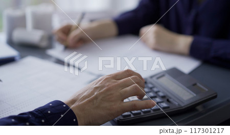 Two unrecognizable accountants or auditors reviewing financial data in office. Professionals analyzing paper reports and using calculator, close up. Audit concept Two unrecognizable accountants or auditors reviewing financial data in office. Professionals analyzing paper reports and using calculator, close up. Audit concept 117301217