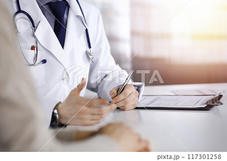 Unknown male doctor and patient woman discussing something while sittingin a darkened clinic, glare of light on the background. Close-up of hands 117301258