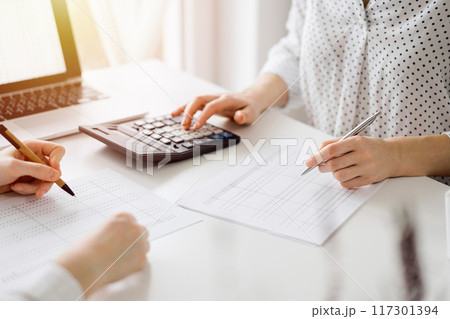 Two accountants using a calculator and laptop computer for counting taxes at white desk in office. Teamwork in business audit and finance 117301394
