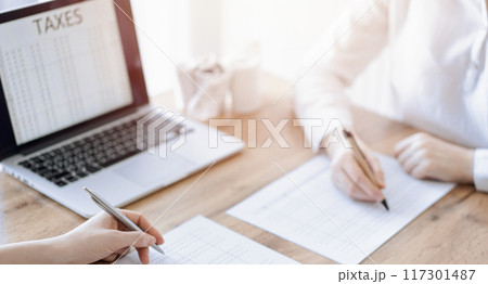 Two accountants using a laptop computer and calculator while counting taxes at wooden desk in office. Teamwork in business audit and finance 117301487