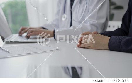 Doctor and a patient in clinic. The female physician is using laptop computer for filling up medication history record form, close up. Medicine and science Doctor and a patient in clinic. The female physician is using laptop computer for filling up medication history record form, close up. Medicine and science 117301575