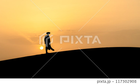Silhouette of an unidentified Berber man in a long robe standing on sand dunes during a stunning sunset in the Sahara Desert, Morocco. 117302908