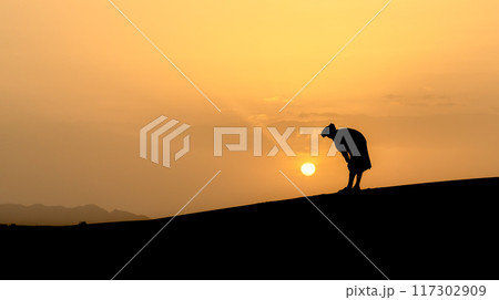 Silhouette of unidentified muslim Berber man praying on sand dunes at beautiful sunset in Sahara Desert, Morocco Silhouette of unidentified muslim Berber man praying on sand dunes at beautiful sunset in Sahara Desert, Morocco 117302909