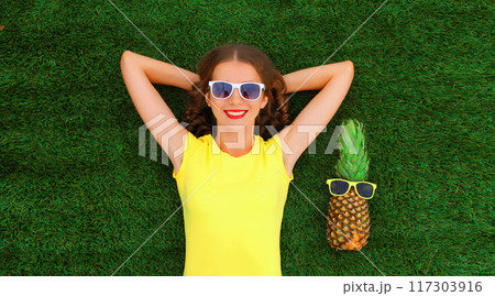Summer portrait of happy smiling young relaxing woman with fruits in glasses lying on the grass Summer portrait of happy smiling young relaxing woman with fruits in glasses lying on the grass 117303916