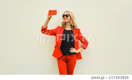 Portrait beautiful smiling elegant lady woman taking selfie with phone wearing red business blazer Portrait beautiful smiling elegant lady woman taking selfie with phone wearing red business blazer 117303926