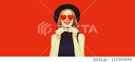 Portrait of beautiful young woman with red heart shaped lollipop in black round hat on background Portrait of beautiful young woman with red heart shaped lollipop in black round hat on background 117303934