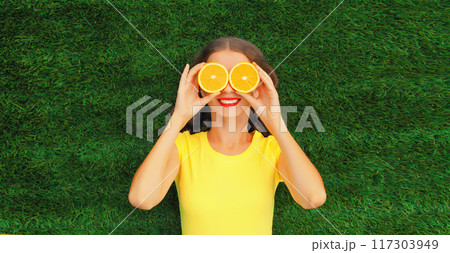 Summer portrait of happy cheerful smiling woman with slices of orange lying on the grass in the park 117303949