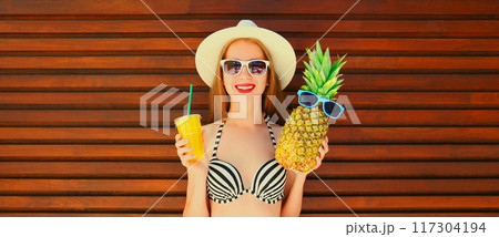 Summer portrait of happy smiling young woman with pineapple, fresh cup of juice wearing summer hat Summer portrait of happy smiling young woman with pineapple, fresh cup of juice wearing summer hat 117304194